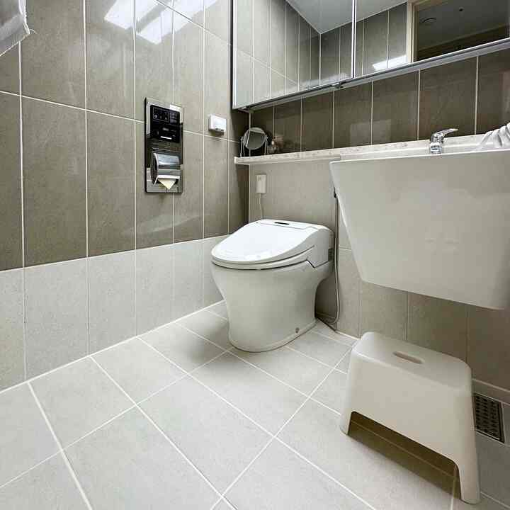 グレーとホワイトのトーンのバスルーム、スマートトイレと一体型の洗面台、白いスツールが配置された清潔でミニマルな印象のインテリア