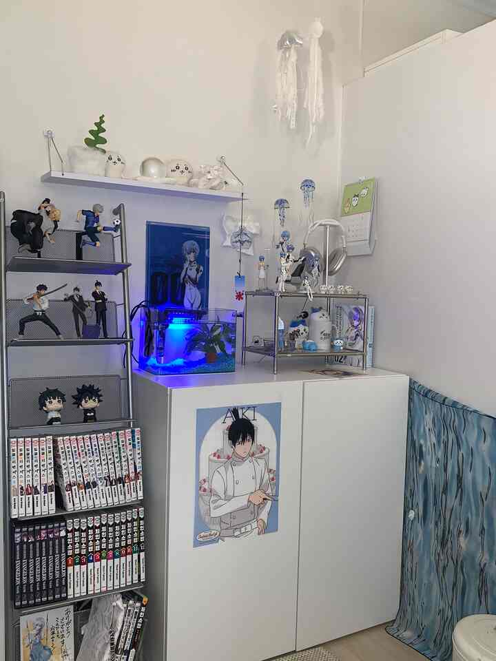 A compact study room with white and blue tones, featuring anime figurines and a colorful bookshelf creating a cozy atmosphere.