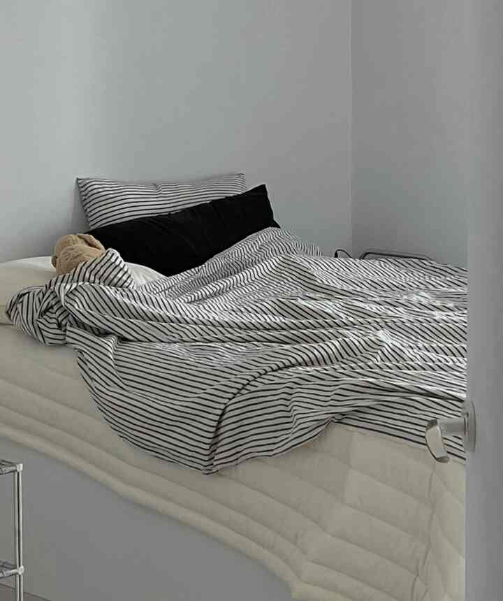 Monotone black and white bedroom featuring a single bed with striped duvet cover centrally placed, showcasing a minimal and modern atmosphere