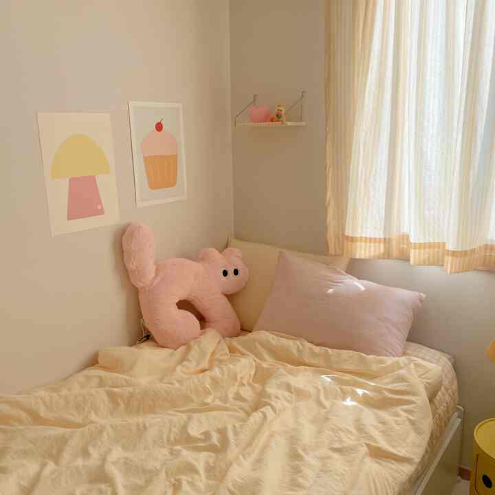 イエローとピンクの色調が優しい子供部屋、枕やぬいぐるみ、かわいいポスターが配置された雰囲気のある寝室