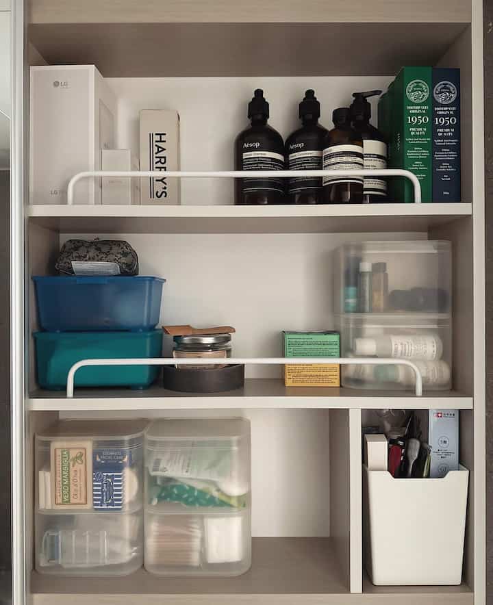 White-toned bathroom shelving featuring neatly organized storage containers and various bathroom products in a simple layout