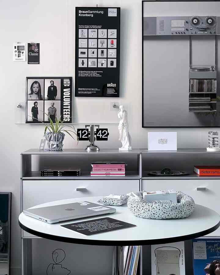 白とグレーのトーンによるシンプルモダンなリビング、丸テーブルと金属棚、額縁とフリップ時計が配置された印象的な空間