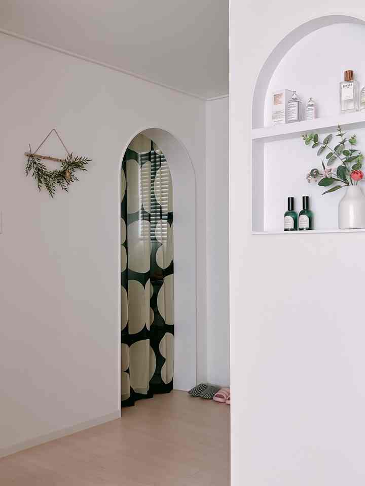 白とベージュのトーンで仕上げられたリビング隣接の狭い空間、アーチ型入り口に柄のカーテンが配置されたナチュラルな雰囲気のインテリア
