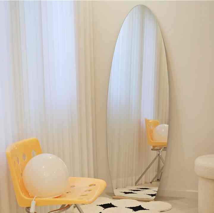 白を基調としたシンプルでモダンな空間、黄色のスツールと全身鏡、モノクロのパターンラグが配置された清潔感のある部屋