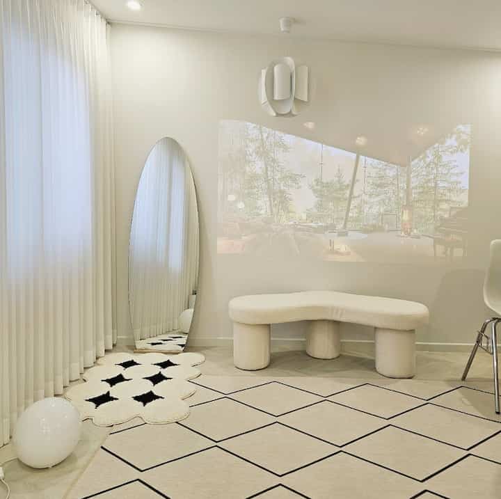 White and beige toned loft featuring an oval full-length mirror, uniquely shaped bench, and geometric patterned rugs in a simple modern interior