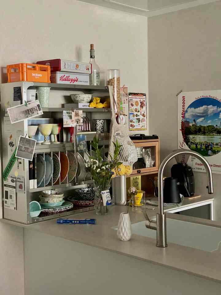 Natural-tone beige walls and white kitchen sink area featuring a metal rack with tableware and coffee equipment in a cozy kitchen space