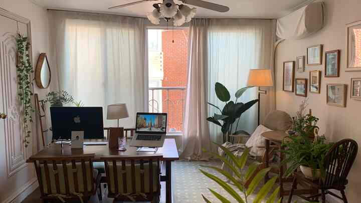 Light beige natural-toned living room with large windows and curtains, wooden furnishings and green plants creating a cozy home office space