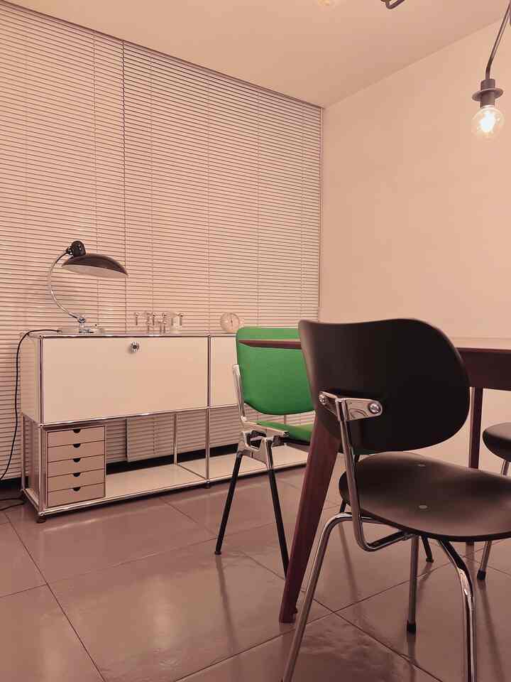 White and beige toned dining room featuring dining table, blinds, and green chairs in a modern setting