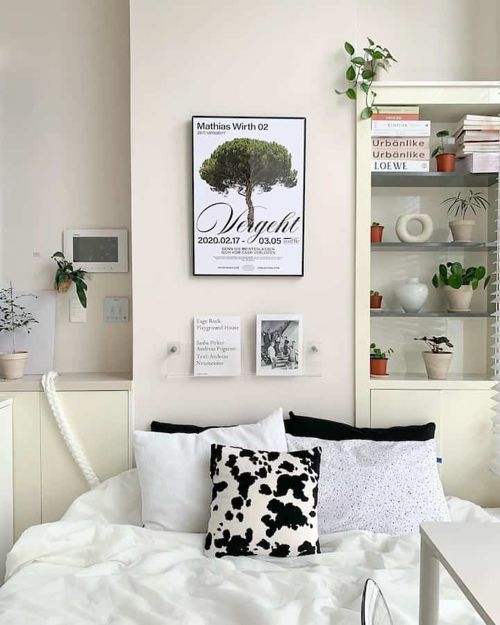 ホワイトとナチュラルカラーの寝室、白い寝具と複数の額縁・植物が配された清潔でモダンな雰囲気のインテリア