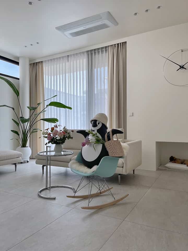 Bright white and beige living room featuring a light blue Eames rocking chair with a penguin objet, creating a natural and modern atmosphere