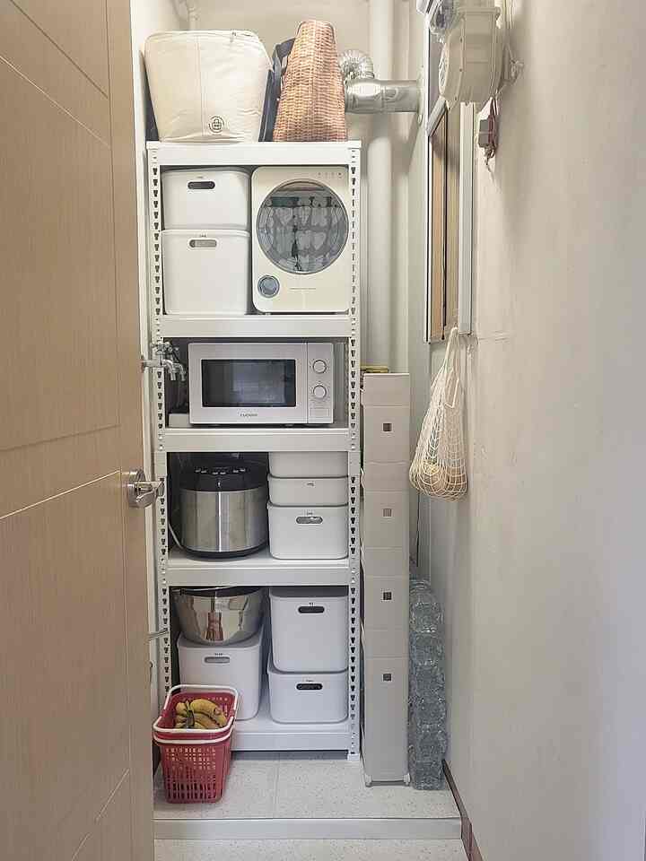 A narrow pantry space in white and beige tones featuring organized storage boxes and a microwave, a practical utility room