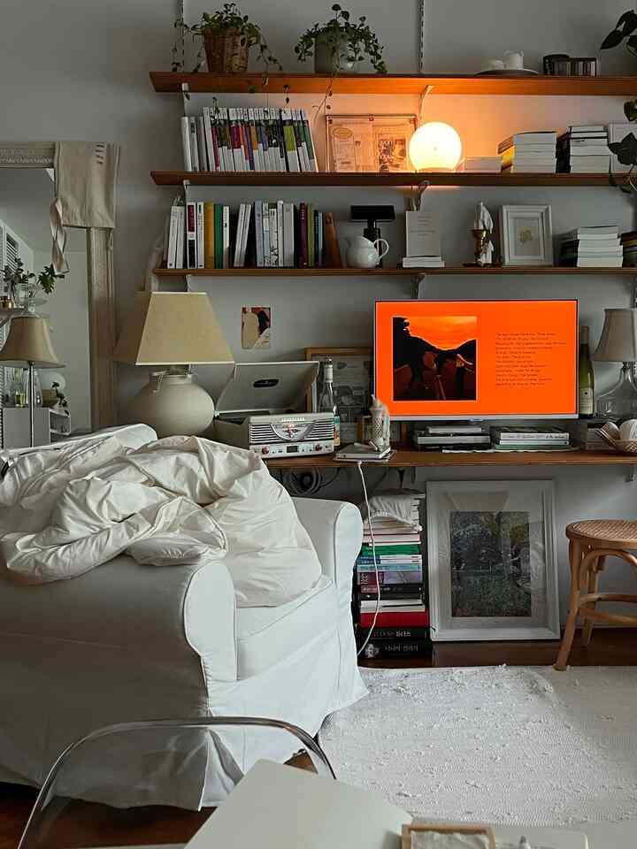 Bright white and natural toned living room featuring a white sofa, TV stand, and bookshelves, creating a cozy and orderly atmosphere