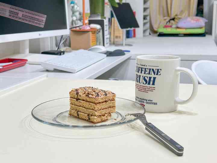 Bright-toned home office space featuring a glass plate with a slice of cake and a coffee mug on a cafe-style table