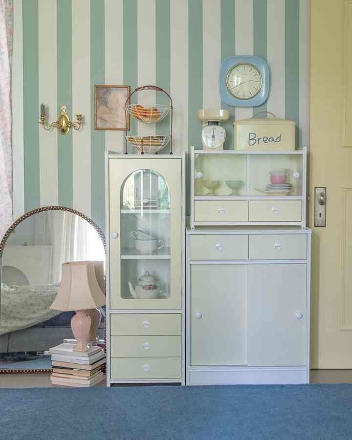 パステルブルーとベージュのストライプ壁のキッチンスペース、ヴィンテージキャビネットと小物が配置された雰囲気のあるインテリア