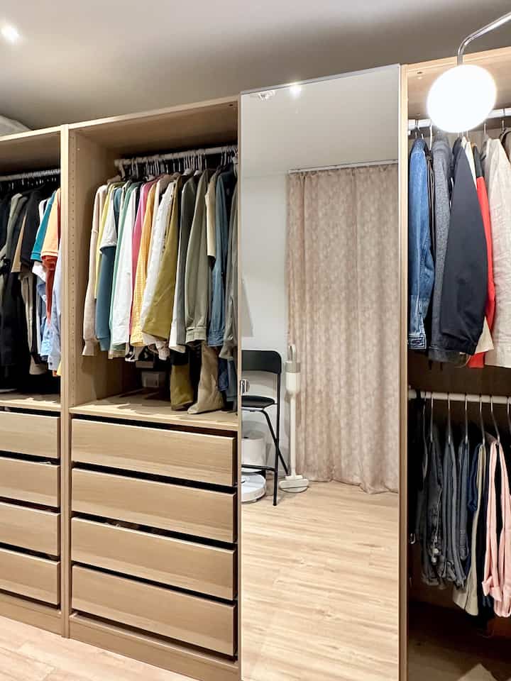 Natural modern closet with light brown wood tone and white background, featuring organized clothes and a wall lamp