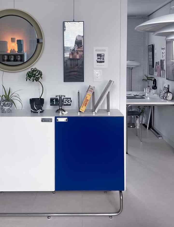 Modern living room in white and blue tones featuring sleek storage cabinet, desk, and plants with a practical and stylish atmosphere