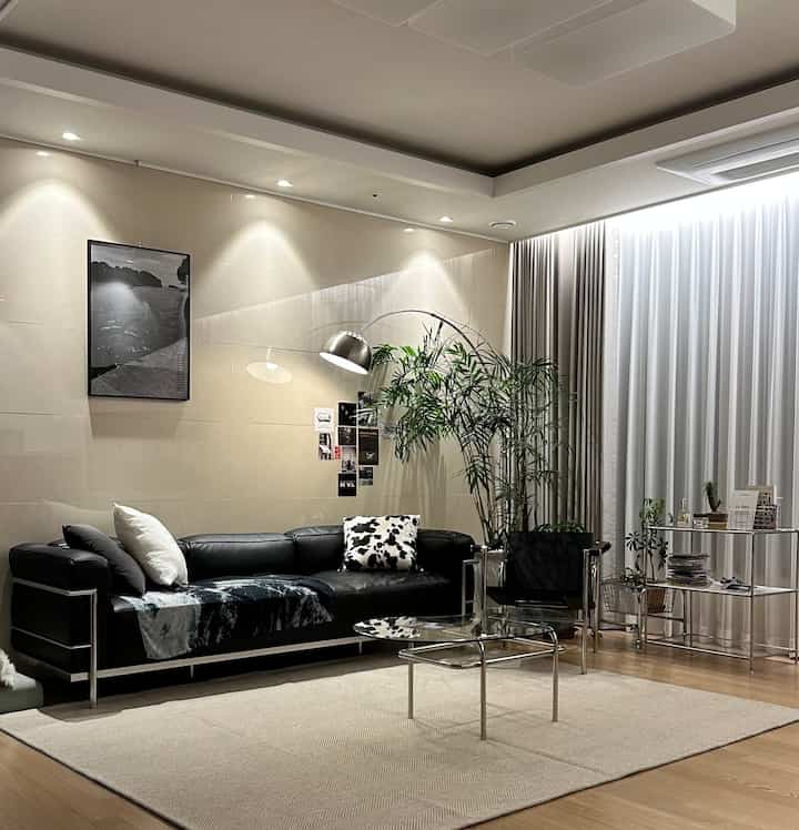 ブラックレザーソファとガラステーブルが配置された明るいミッドセンチュリーモダンのリビングルーム