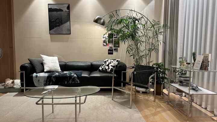 ブラックとベージュの調和が美しいミッドセンチュリーモダンのリビング、レザーソファとガラステーブル、豊かな植物が配置された落ち着いた空間