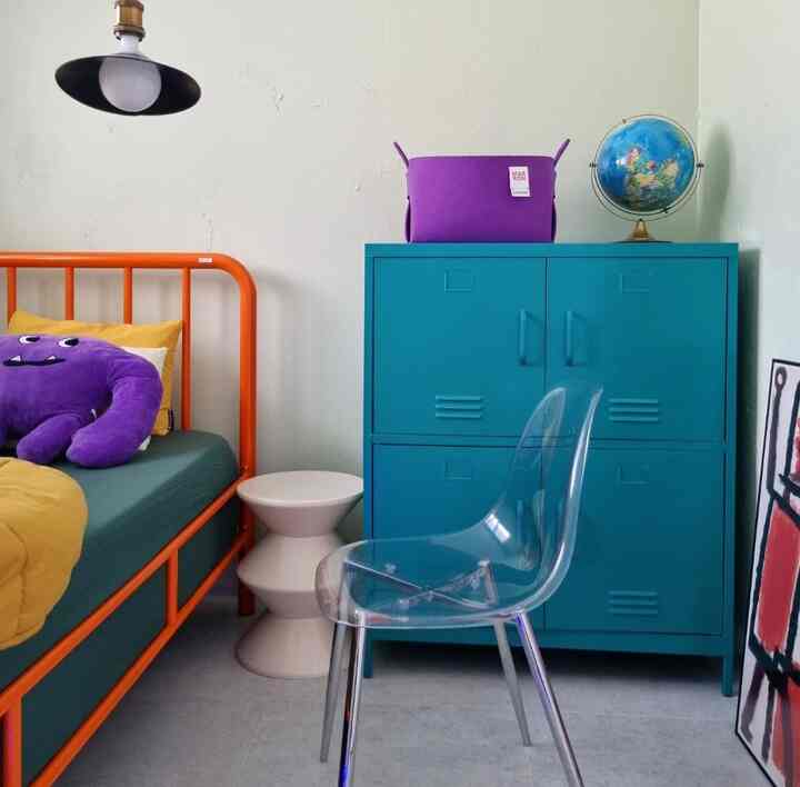 鮮やかなオレンジ色の鉄製ベッドと青い収納キャビネットが配置された子供部屋の印象的な空間