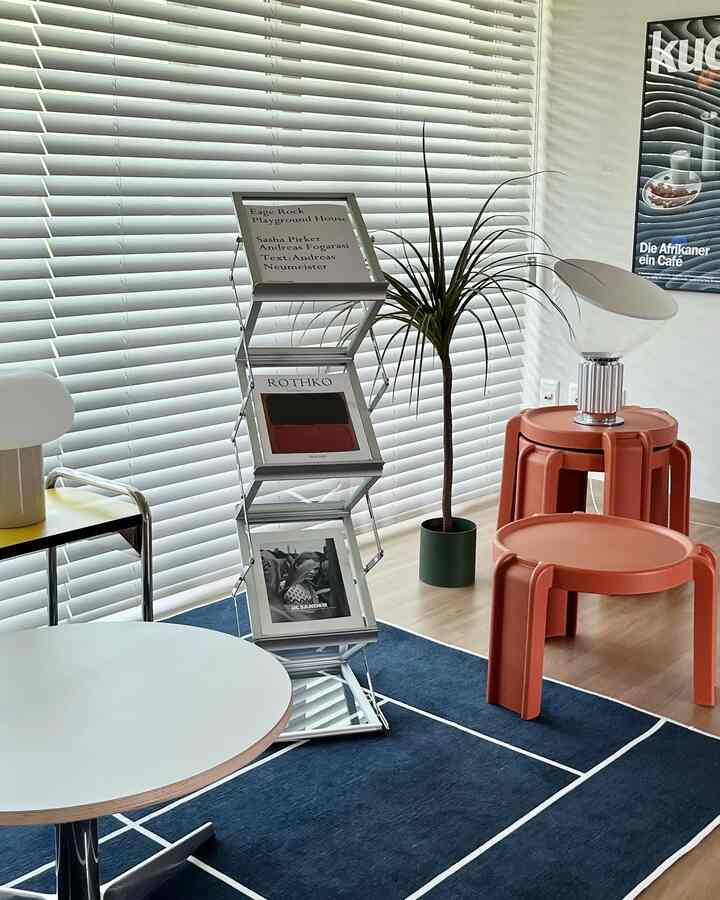 Mid-Century Modern living space in white and navy tones featuring a central metal magazine rack and orange side tables with cafe-style ambiance