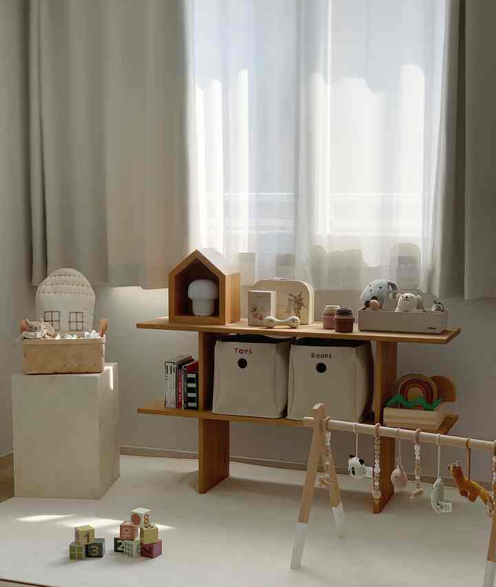 温かみのあるベージュとナチュラルトーンの子供部屋、ムードある遮光カーテンとシフォンカーテン、木製のおもちゃ収納が配置された居心地の良い空間