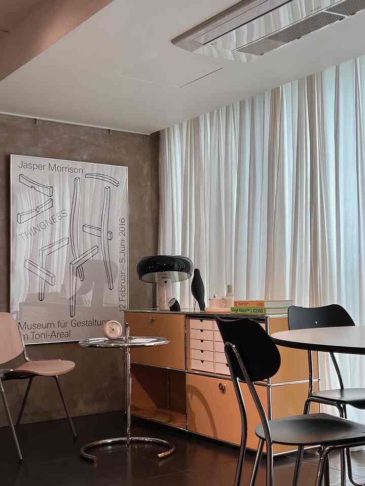 A sophisticated living room with brown textured walls, white curtains, Mid-Century Modern USM storage, and black chairs