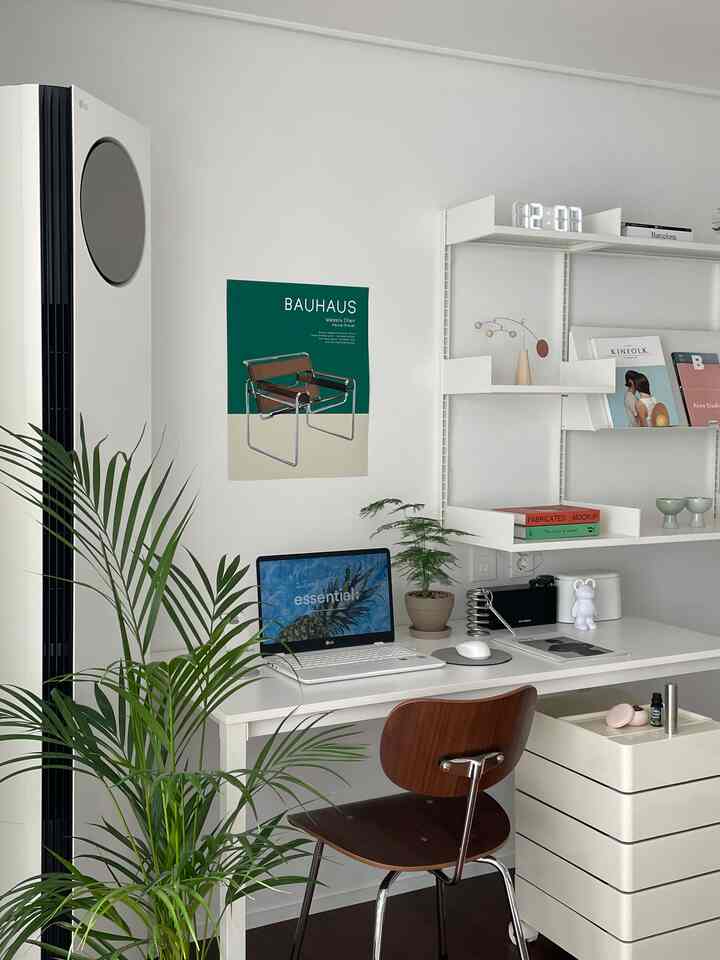 White-toned living room home office featuring a white desk, brown chair, and shelves with decor in a simple interior