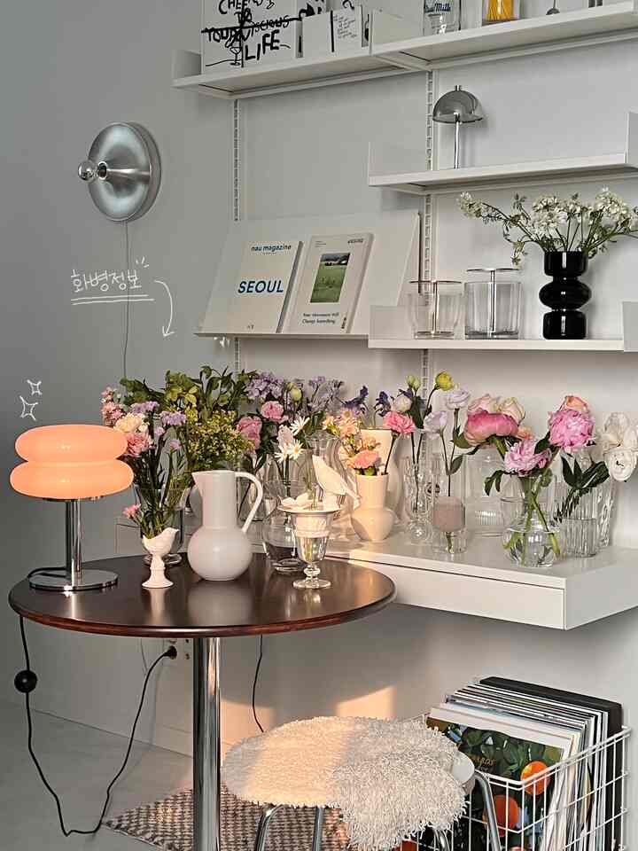 ホワイトとブラウンのトーンでまとめられた小さなテーブルと多彩な花瓶が配置されたミニマルな印象の室内空間