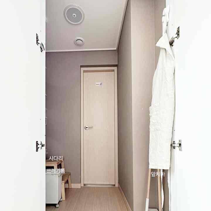 Minimal storage area in a narrow hallway with white and beige tones featuring a hanging apron on suction hooks