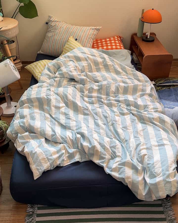 Bedroom featuring blue and white striped bedding with wooden nightstand and an orange lamp creating a cozy atmosphere