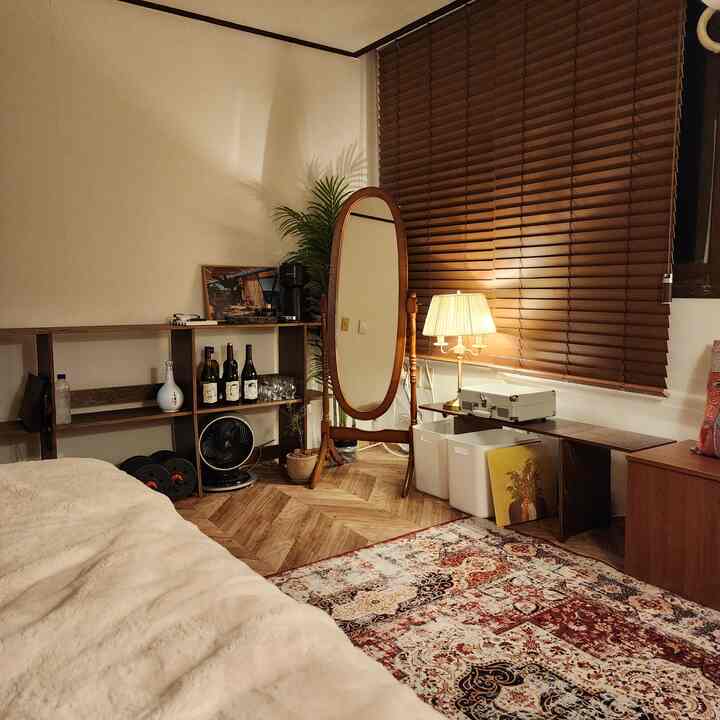 温かみのある木目調とベージュの寝室、木製の全身鏡とペルシャ柄ラグが配置された印象的な空間