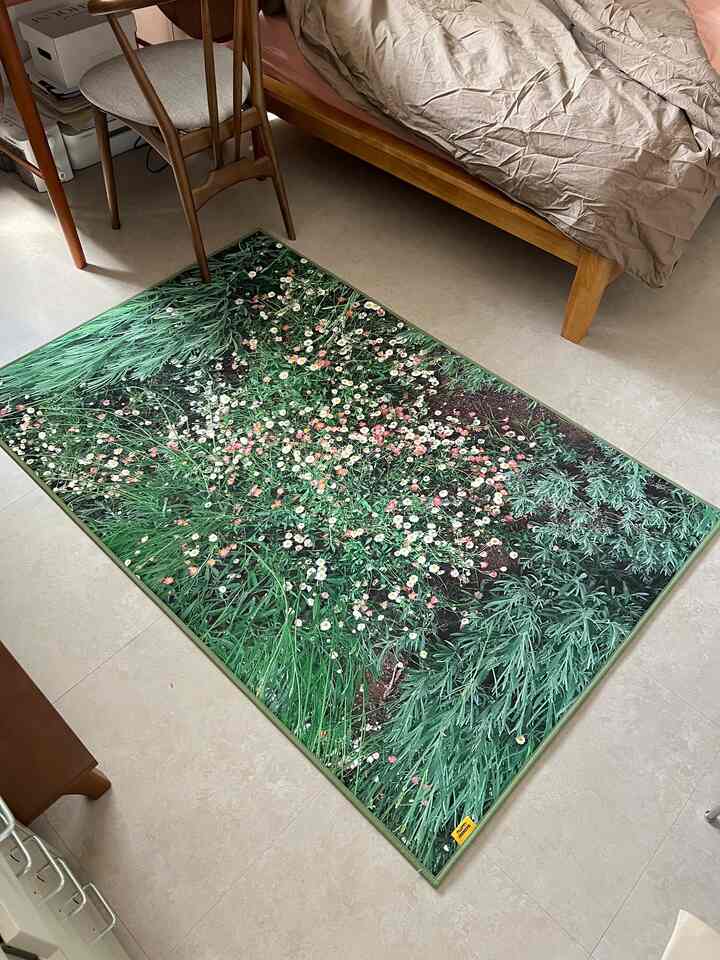 緑色を基調としたワンルーム寝室、花柄のショートパイルラグと木製ベッド、ダイニングチェアが配置された自然で落ち着いたインテリア