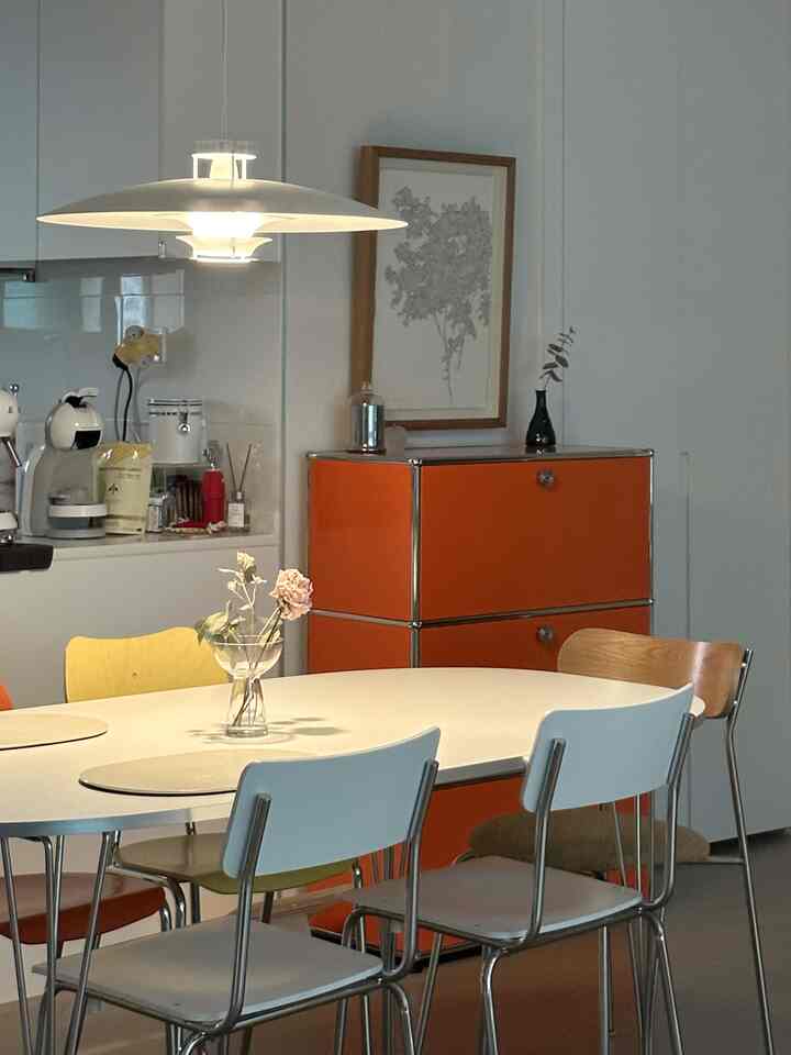 Modern kitchen with white and orange tones, featuring dining table with colorful chairs in a neat setting