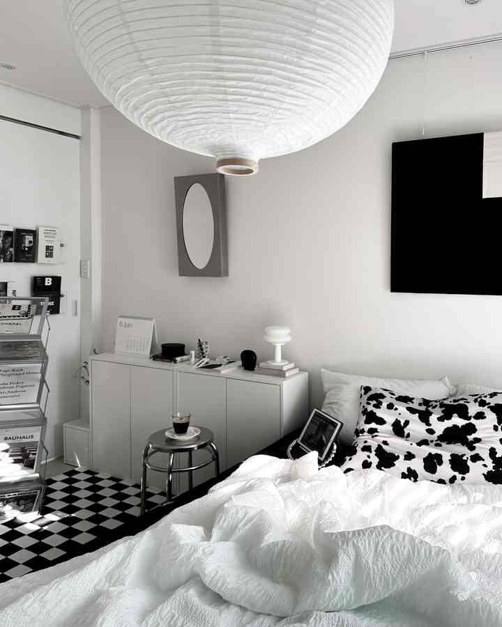Monotone black and white bedroom featuring a white bed with black patterned pillows, stainless stool with coffee, and mid-century modern lamp creating a simple modern interior.