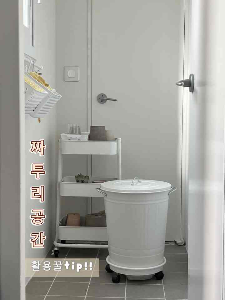 A white and gray toned dead space featuring a mobile trolley and trash can arranged neatly in a practical storage area
