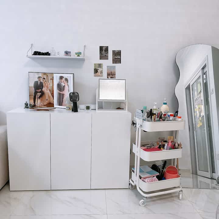 A clean living room space dominated by white tones, featuring a trolley, storage unit, and irregular-shaped full-length mirror