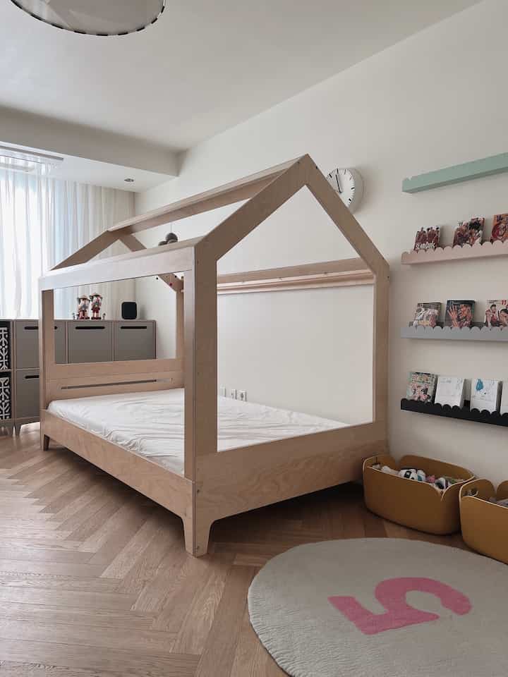 Clean kids' room with white walls and natural wood-tone flooring and bed, featuring cloud shelves and storage bins with cozy atmosphere