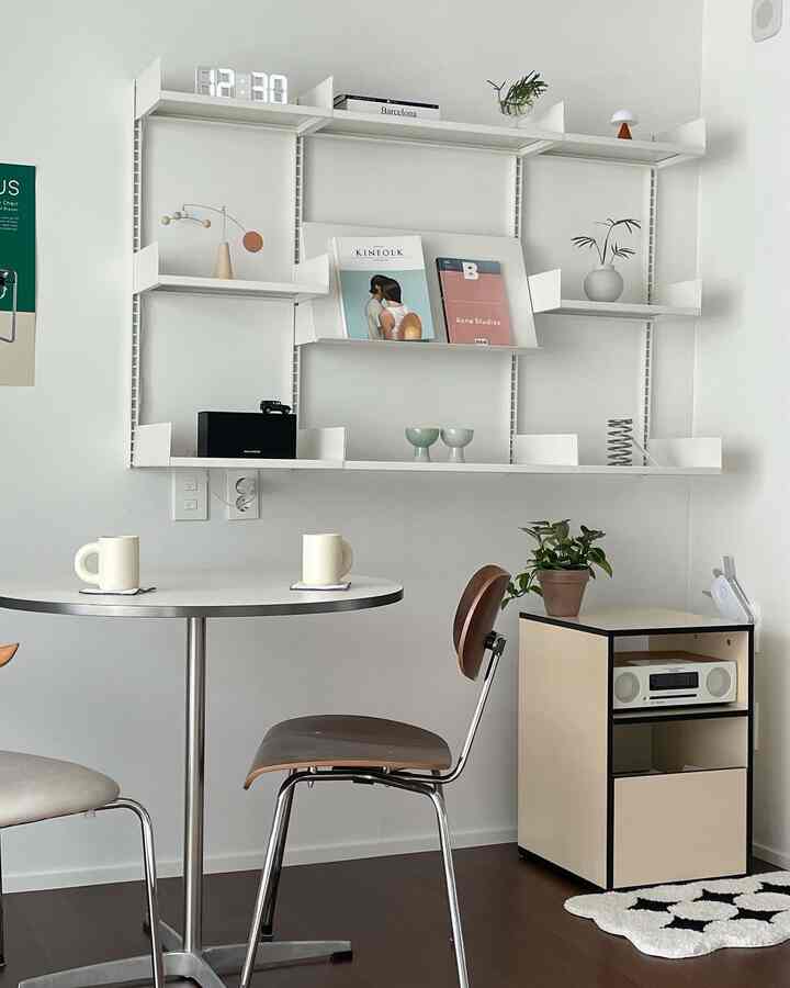 White-toned dining room featuring mid-century modern chairs, shelving, and coffee mugs on a round table creating a clean atmosphere