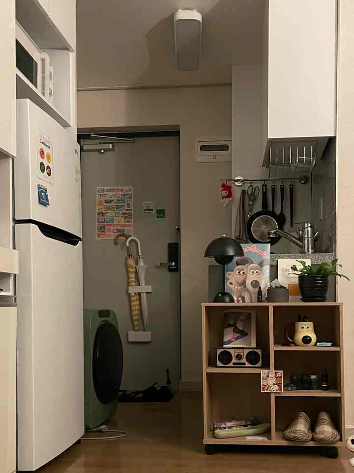 白と木目調の玄関兼キッチン、キャビネットの上にオブジェやミニマルな小物が配置された雰囲気あるインテリア