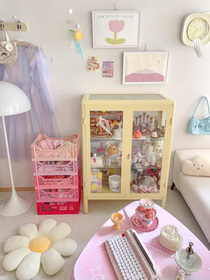 Pastel-toned baby room or home cafe space featuring a yellow cabinet, pink storage boxes, wall decor, and a clock creating a cozy atmosphere