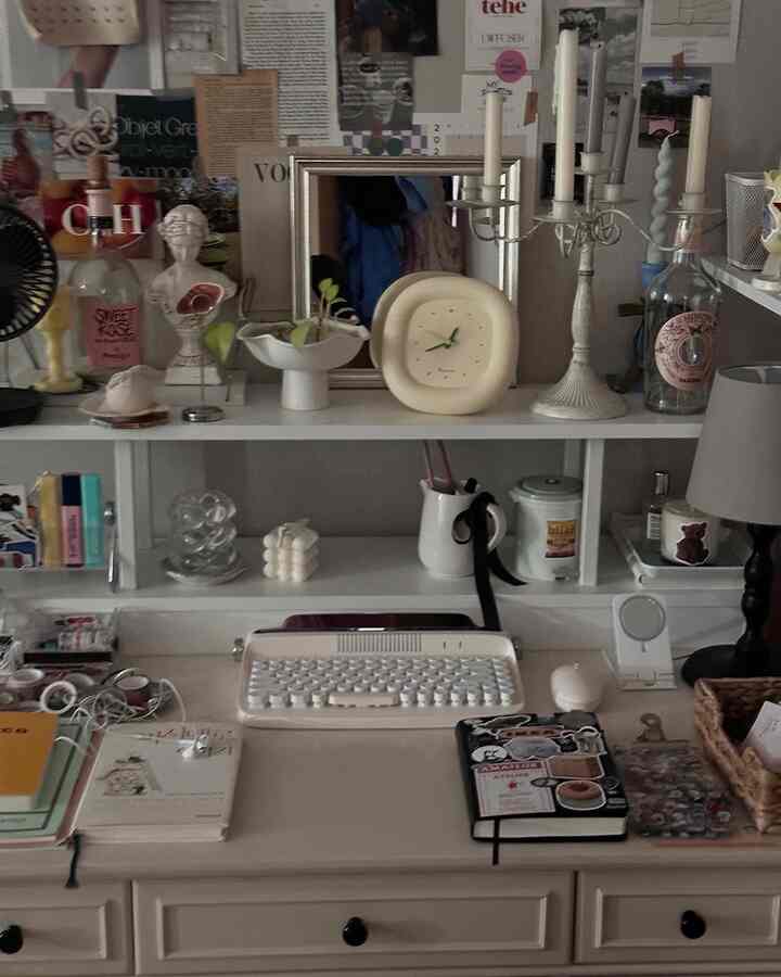 A white and beige toned home office featuring a desk and bookshelf, adorned with various candles and objets creating a cozy atmosphere