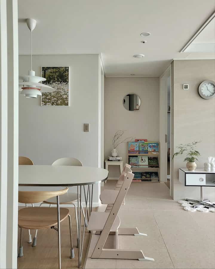 Natural wood tone and beige living room featuring dining table, chairs, and kids' bookshelf in a tidy interior