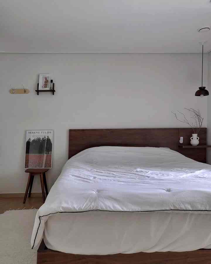 Minimal bedroom in white and wood tones featuring a wooden bed, stool, and posters creating a neat and calm atmosphere