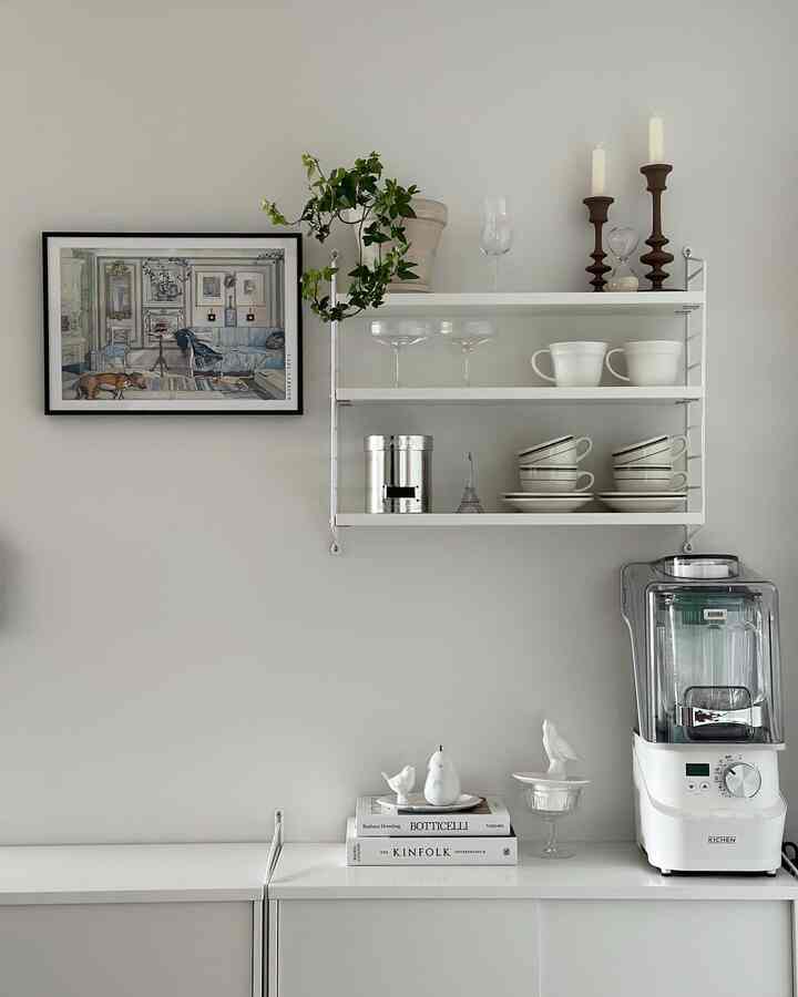 Modern Nordic kitchen space with white walls and shelves, neatly arranged cups and a blender showcasing clean interior