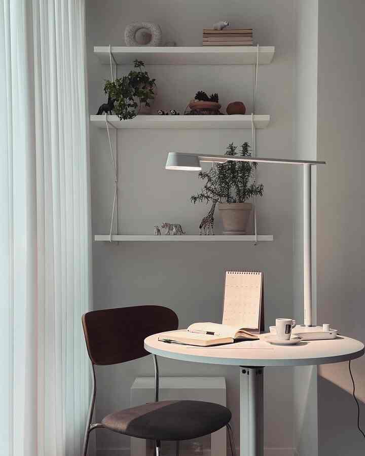 白を基調とした壁に棚が配置されたホームオフィス空間、丸テーブルと椅子がシンプルなモダンさを演出している