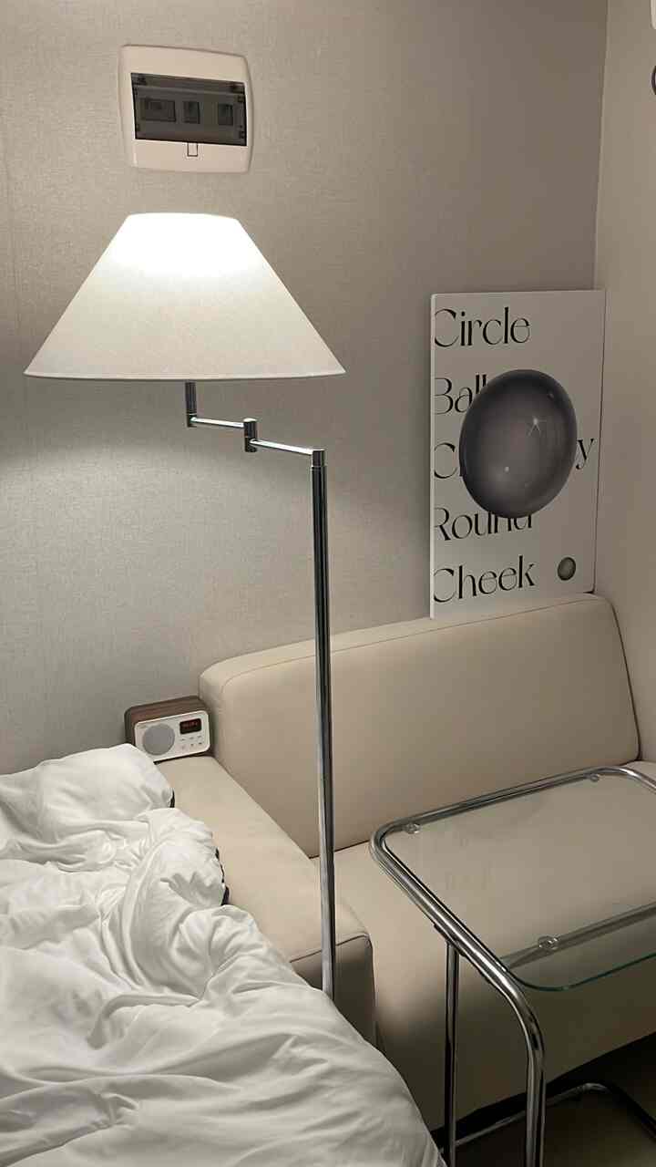 ホワイトとベージュのトーンのワンルーム寝室、フロアランプとソファ、サイドテーブルが調和した落ち着いた空間