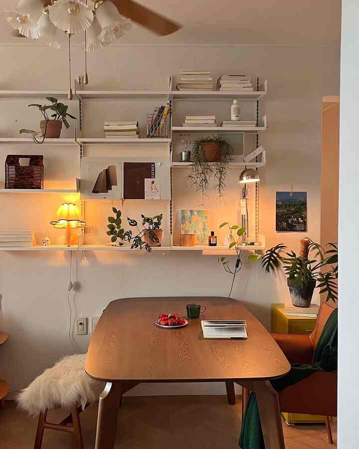 Natural wood tone living room featuring a walnut dining table, armchair, and shelves with plants creating a cozy atmosphere