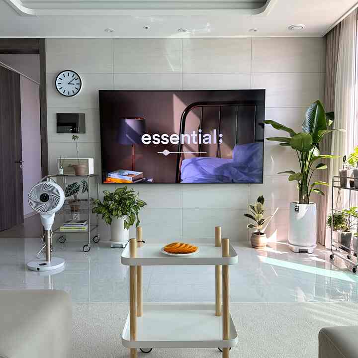 A bright, clean living room in white and green tones featuring modern furniture and various indoor plants