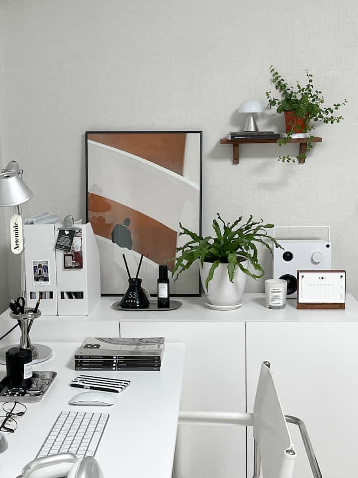 White-toned home office space featuring a clean desk and chair, poster frame, and plants in a minimal interior