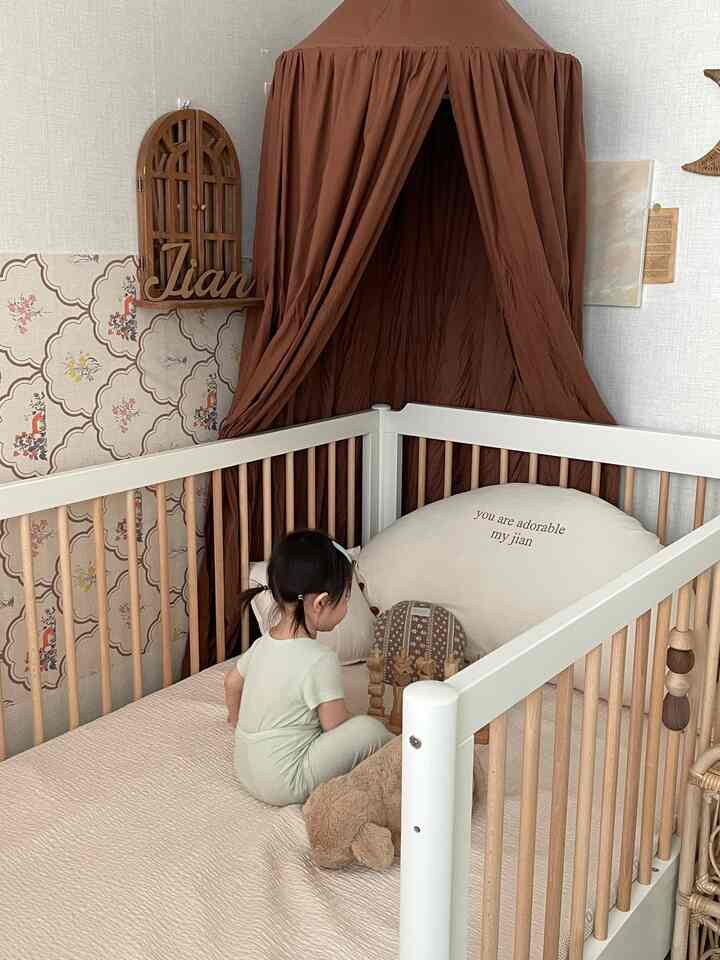 ベージュとブラウンの色調の子供部屋、木製のベッドとブラウンのキャノピーが配置された温かみのある自然なインテリア